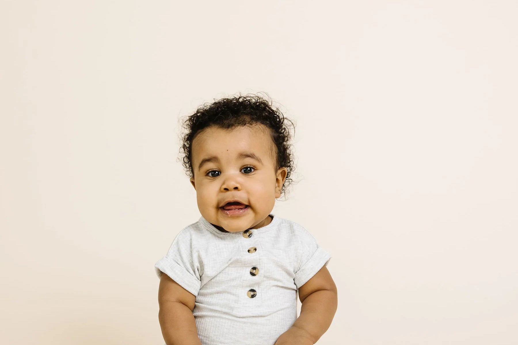 Baby sitting up wearing the Lou Lou & Company Ribbed Romper in Stevie gray