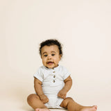 Baby sitting up wearing the Lou Lou & Company Ribbed Romper in Stevie gray