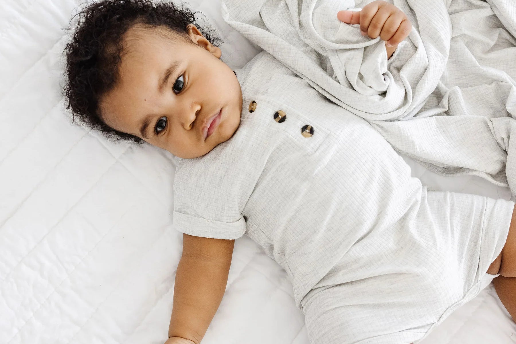 Baby lying on a white blanket in the Lou Lou & Company Ribbed Romper in Stevie gray, from above