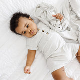 Baby lying on a white blanket in the Lou Lou & Company Ribbed Romper in Stevie gray, from above