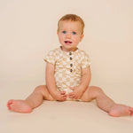 Smiling baby sitting in the Lou Lou & Company Romper in Austin checkered print