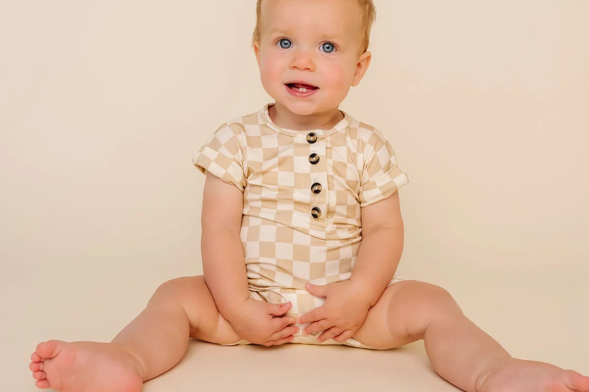 Smiling baby sitting in the Lou Lou & Company Romper in Austin checkered print