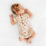 Newborn with a bow lying on a blanket in the Lou Lou & Company Romper in Rachel floral