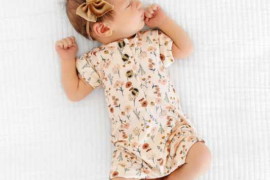 Newborn with a bow lying on a blanket in the Lou Lou & Company Romper in Rachel floral