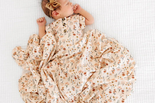 Newborn in the Lou Lou & Company Romper in Rachel lying on a matching floral swaddle