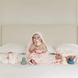 Baby in a pink hooded towel sitting on a bed with the Lou Lou & Company Rubber Duckies Set