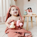 Smiling baby in a pink hooded towel holding Lou Lou & Company Rubber Duckies in a nursery