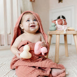 Smiling baby in a pink hooded towel holding Lou Lou & Company Rubber Duckies in a nursery