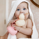 Baby in a hooded towel chewing on a cream Lou Lou & Company Rubber Ducky and holding a pink one