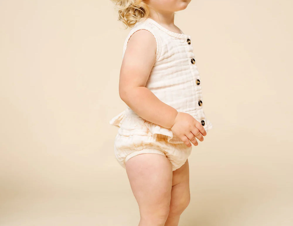 Toddler standing sideways wearing the Lou Lou & Company Ruffle Tank and Bloomer Set in Cream