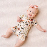 Smiling baby with a pink bow lying in the Lou Lou & Company Shortie Set in Nellie floral