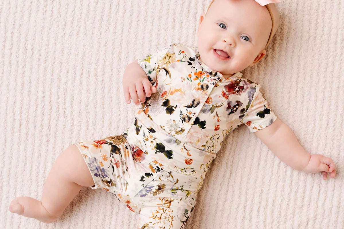 Smiling baby with a pink bow lying in the Lou Lou & Company Shortie Set in Nellie floral