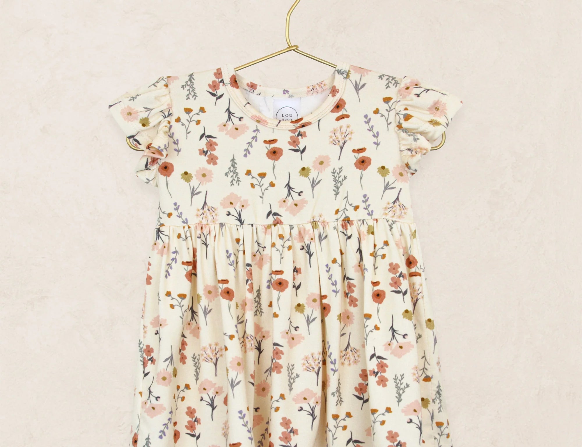 Lou Lou & Company Twirl Dress in Rachel, a cream floral flutter-sleeve dress on a hanger