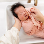 Newborn being washed in a sink with a Lou Lou & Company Washcloth in Blush