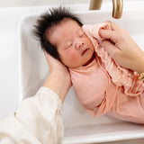 Newborn being washed in a sink with a Lou Lou & Company Washcloth in Blush
