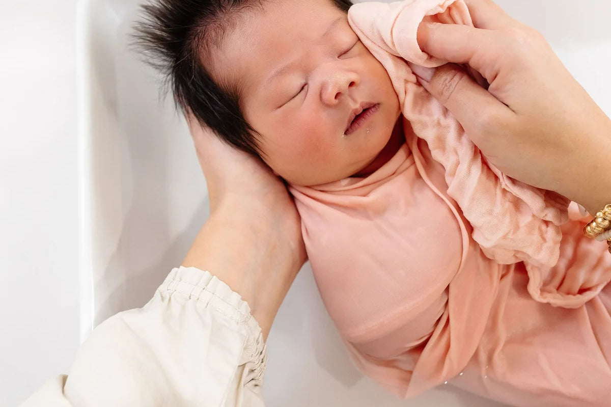 Newborn being washed in a sink with a Lou Lou & Company Washcloth in Blush