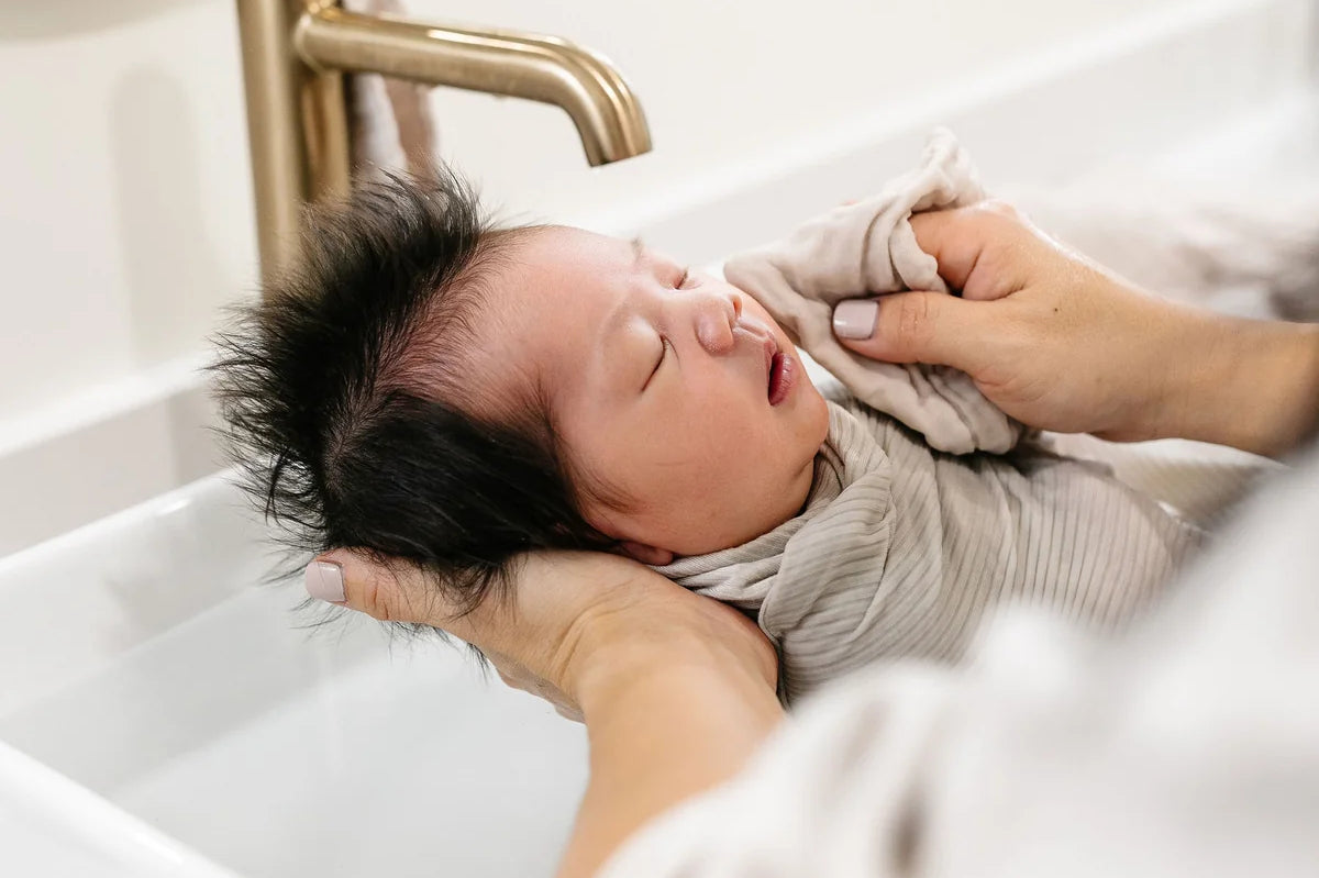 Newborn being bathed in a sink with a Lou Lou & Company Washcloth in Grey