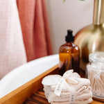 Rolled Lou Lou & Company Washcloths in Grey and Blush on a wooden bath tray with soap