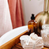 Rolled Lou Lou & Company Washcloths in Grey and Blush on a wooden bath tray with soap