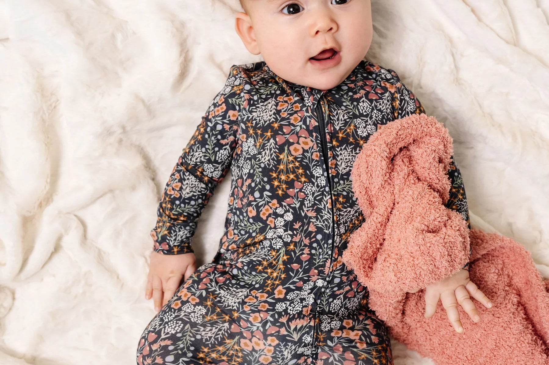 Baby with a pink bow wearing the Lou Lou & Company Zipper Footies in Bae, a navy floral print footie