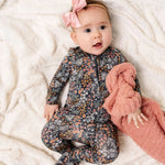 Baby with a pink bow wearing the Lou Lou & Company Zipper Footies in Bae, a navy floral print footie
