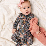 Baby with a pink bow wearing the Lou Lou & Company Zipper Footies in Bae, a navy floral print footie