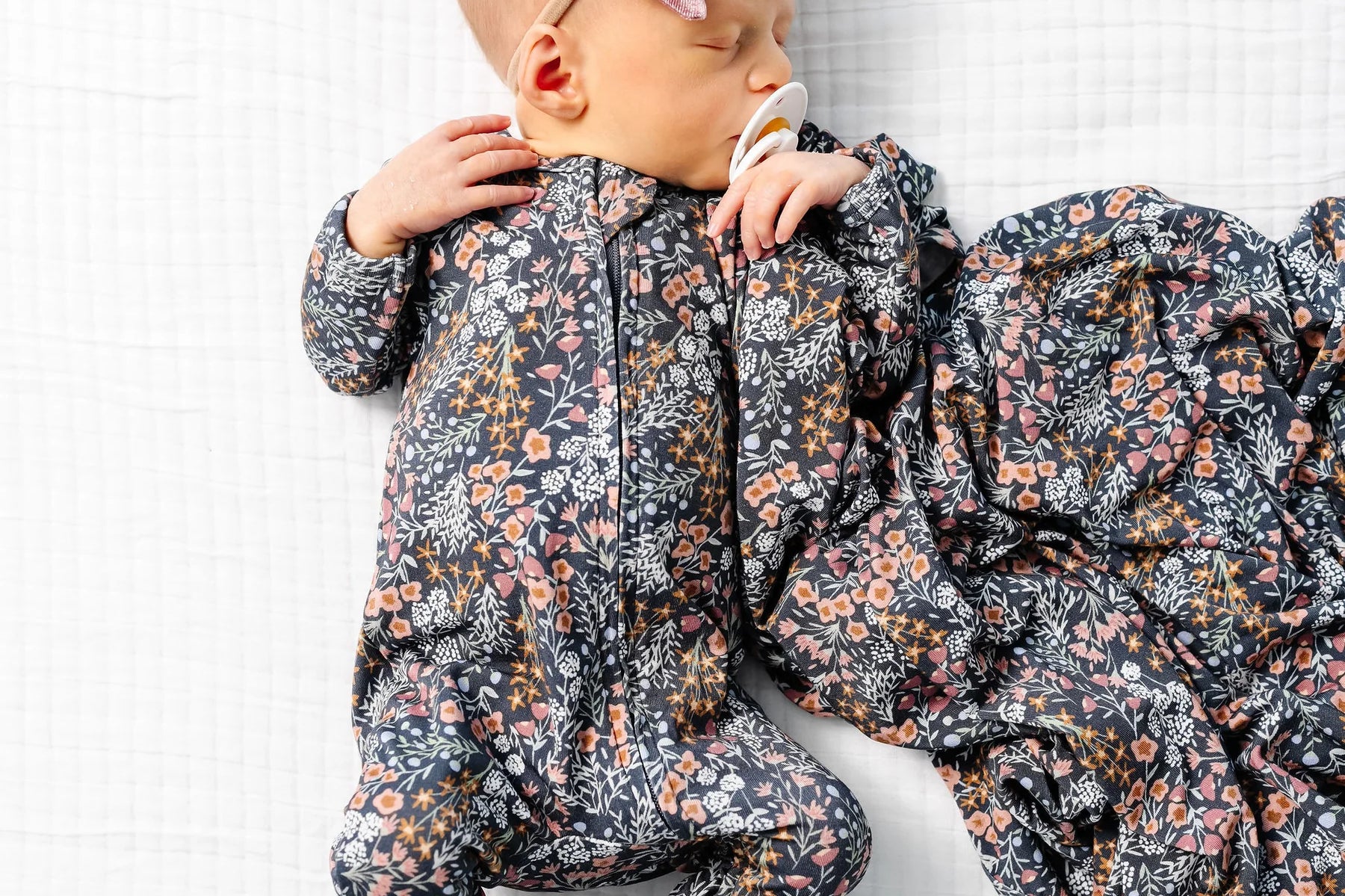 Baby lying on a blanket wearing the Lou Lou & Company Zipper Footies in Bae with a matching floral swaddle