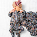 Baby lying on a blanket wearing the Lou Lou & Company Zipper Footies in Bae with a matching floral swaddle