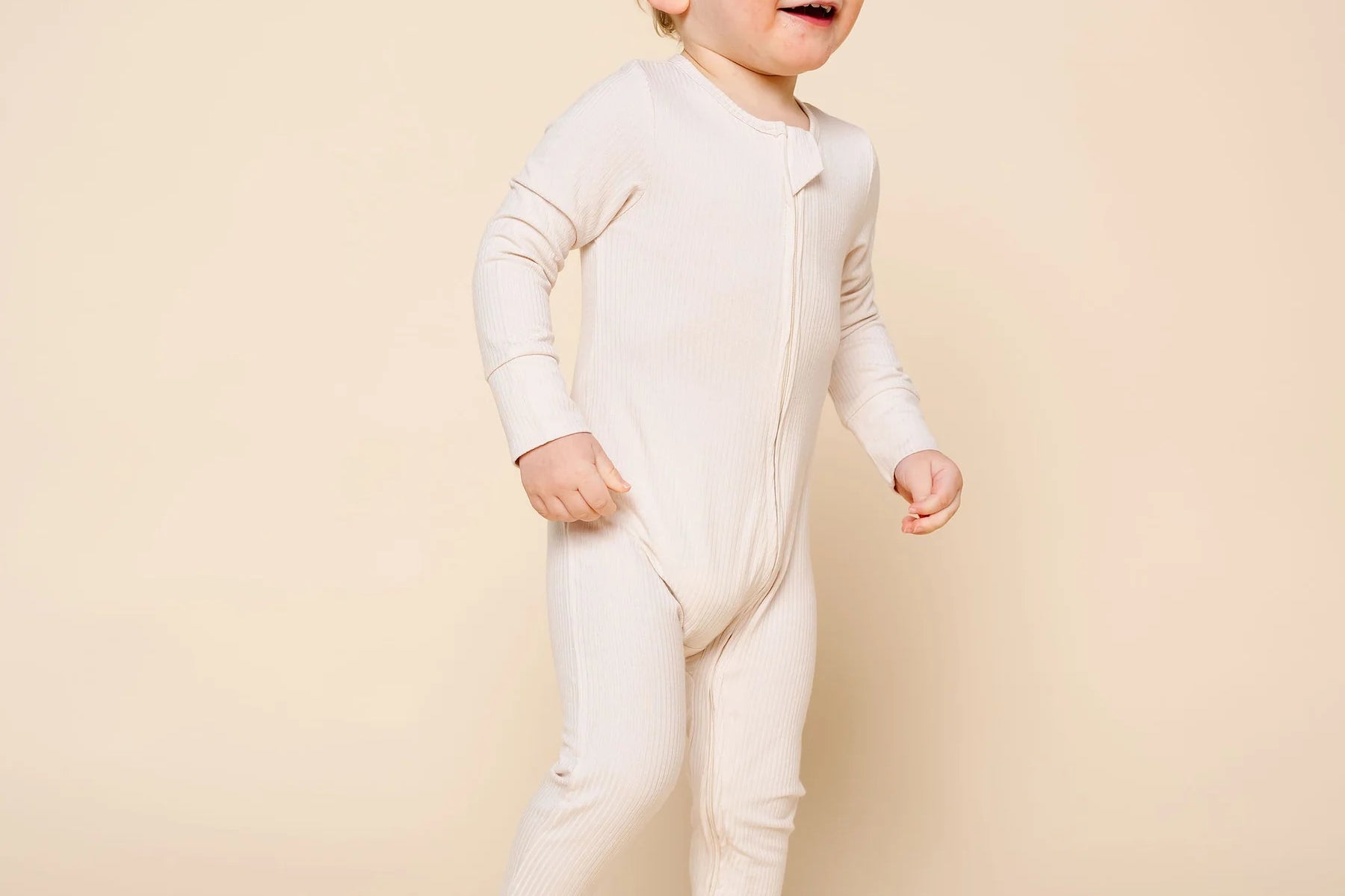 Toddler standing and smiling wearing the Lou Lou & Company Zipper Footies in Cove, a cream ribbed footie