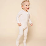 Toddler standing and smiling wearing the Lou Lou & Company Zipper Footies in Cove, a cream ribbed footie