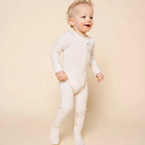Toddler standing and smiling wearing the Lou Lou & Company Zipper Footies in Cove, a cream ribbed footie