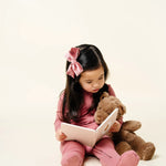 Toddler reading a book with a teddy bear wearing the Lou Lou & Company Zipper Footies in Marjoire