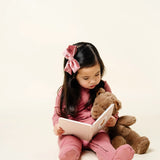 Toddler reading a book with a teddy bear wearing the Lou Lou & Company Zipper Footies in Marjoire
