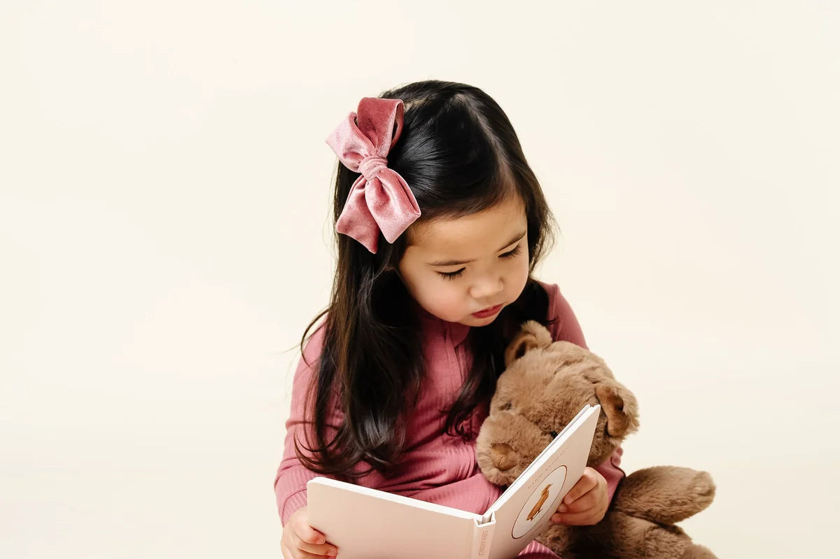 Toddler reading a book with a teddy bear wearing the Lou Lou & Company Zipper Footies in Marjoire
