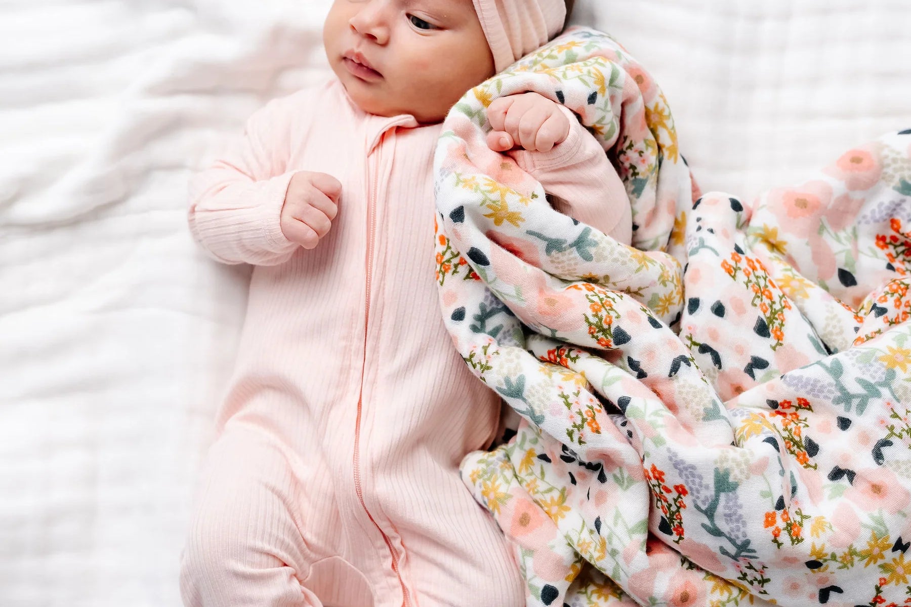 Newborn wearing the Lou Lou & Company Zipper Footies in Rosie, a light pink footie, beside a Bae floral blanket