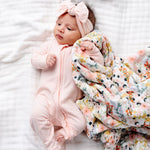Newborn wearing the Lou Lou & Company Zipper Footies in Rosie, a light pink footie, beside a Bae floral blanket