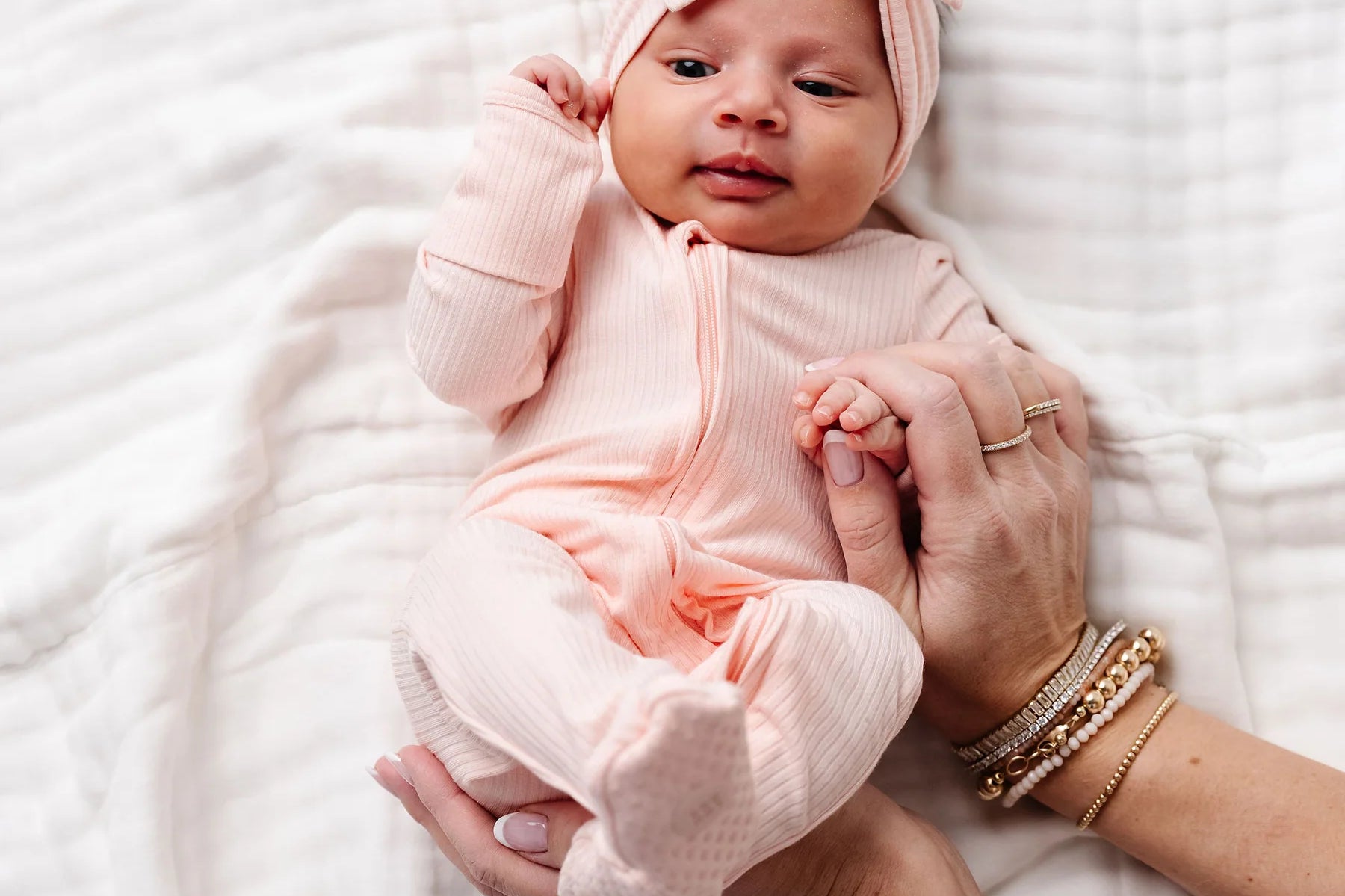 Newborn with a pink bow being held wearing the Lou Lou & Company Zipper Footies in Rosie