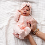 Newborn with a pink bow being held wearing the Lou Lou & Company Zipper Footies in Rosie