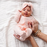 Newborn with a pink bow being held wearing the Lou Lou & Company Zipper Footies in Rosie