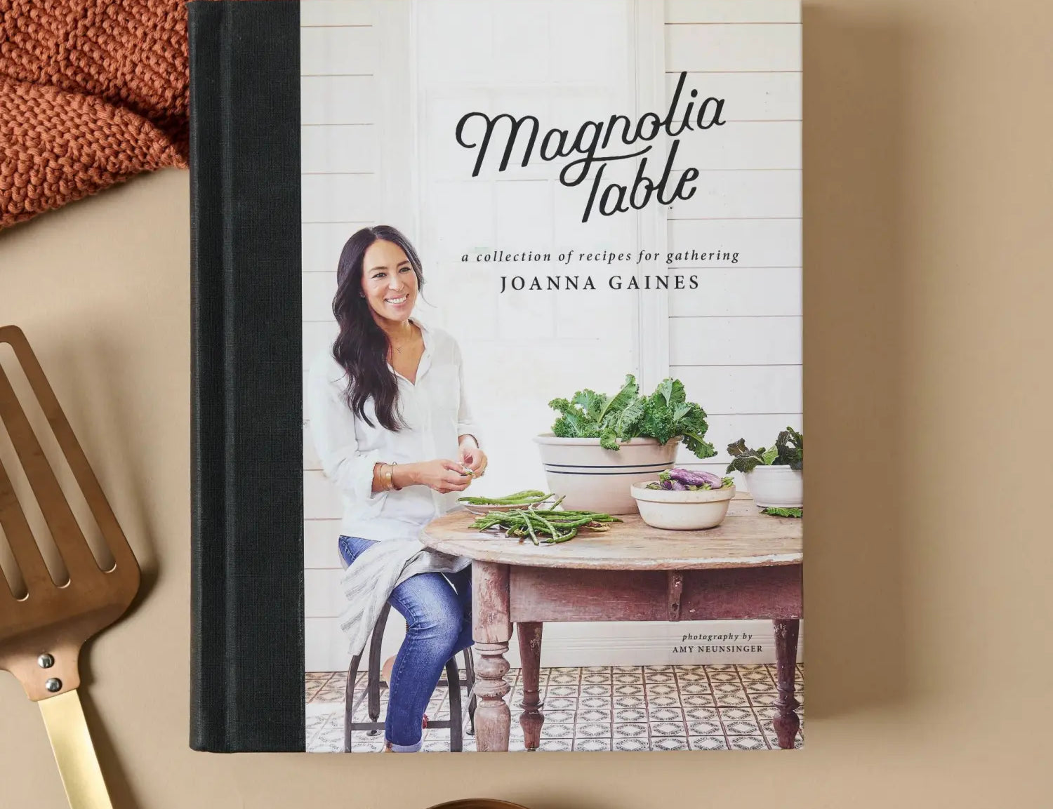 Magnolia Table Cookbook Volume 1 by Joanna Gaines, cover with Joanna at a kitchen table, beside a copper spatula