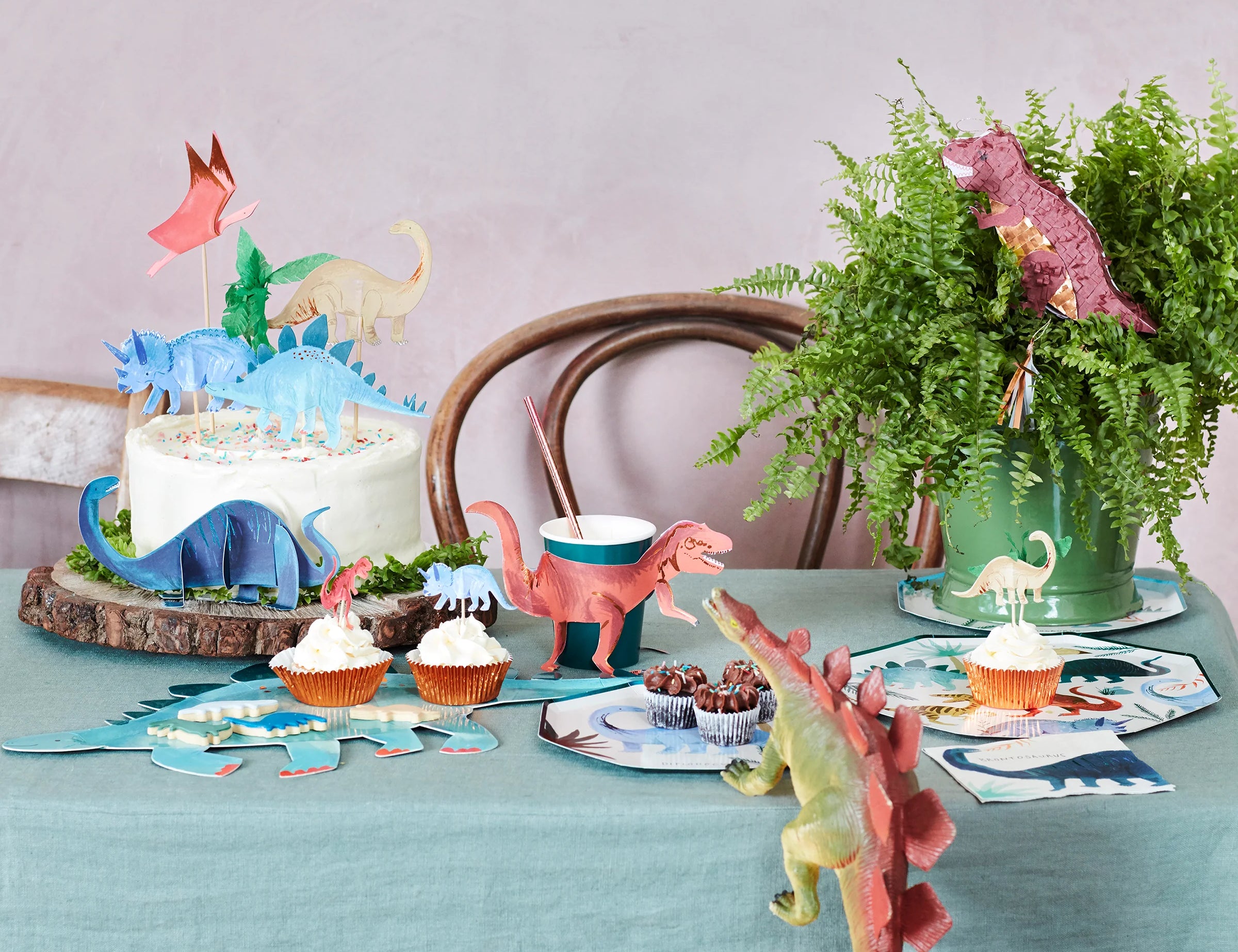 Dinosaur-themed party table with a cake, Meri Meri Dinosaur Kingdom cupcakes and plates