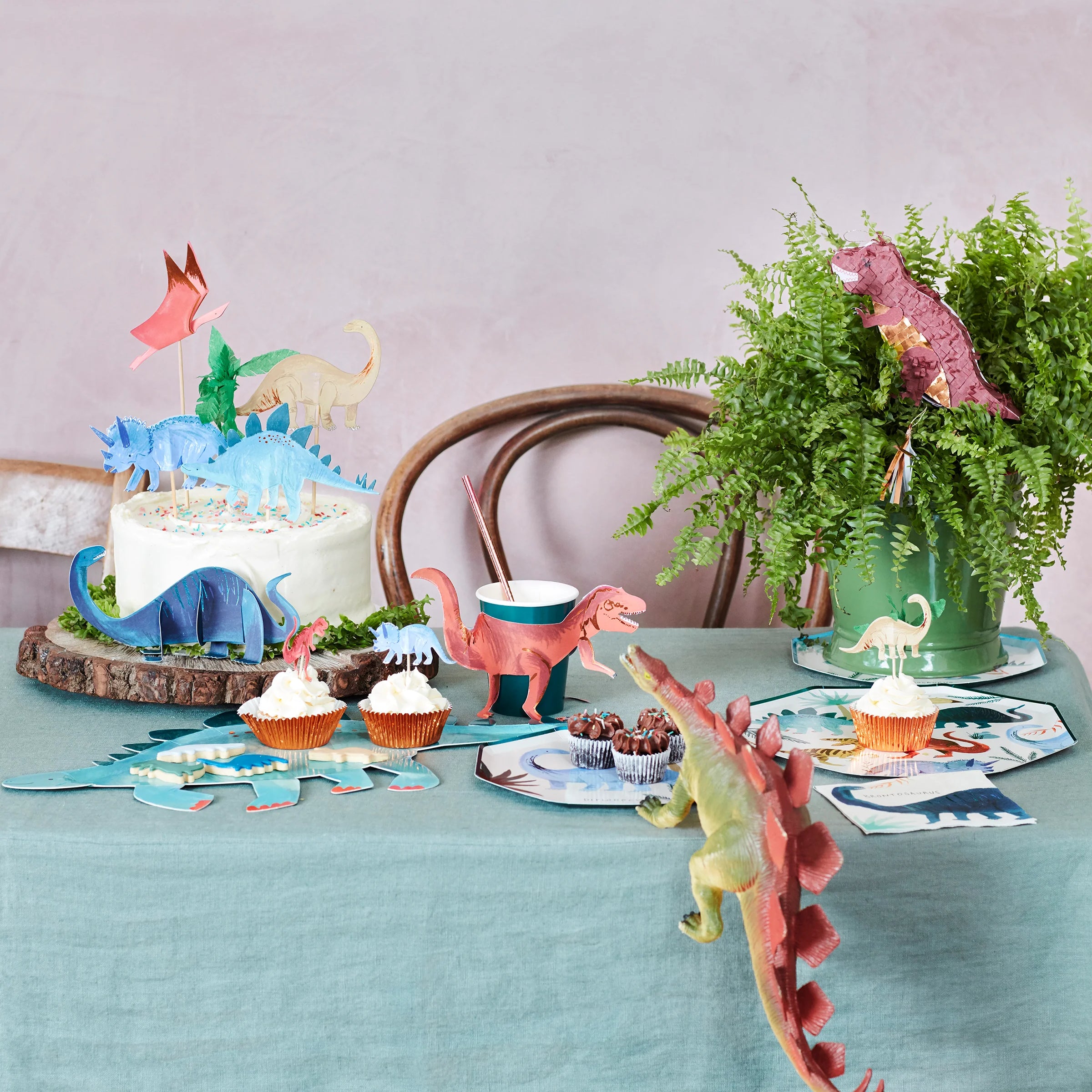 Dinosaur-themed party table with a cake, Meri Meri Dinosaur Kingdom cupcakes and plates