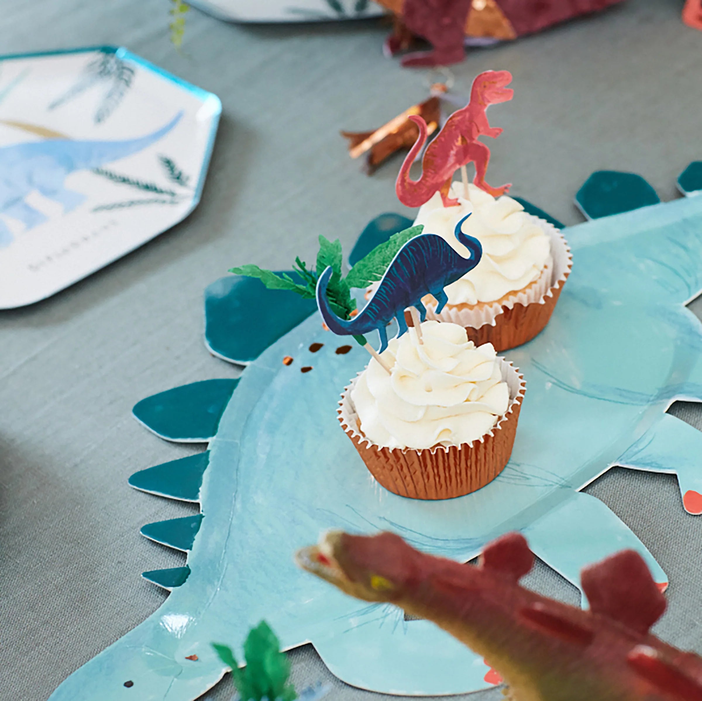 Meri Meri Dinosaur Kingdom Cupcake Kit cupcake on a dinosaur plate at a party table
