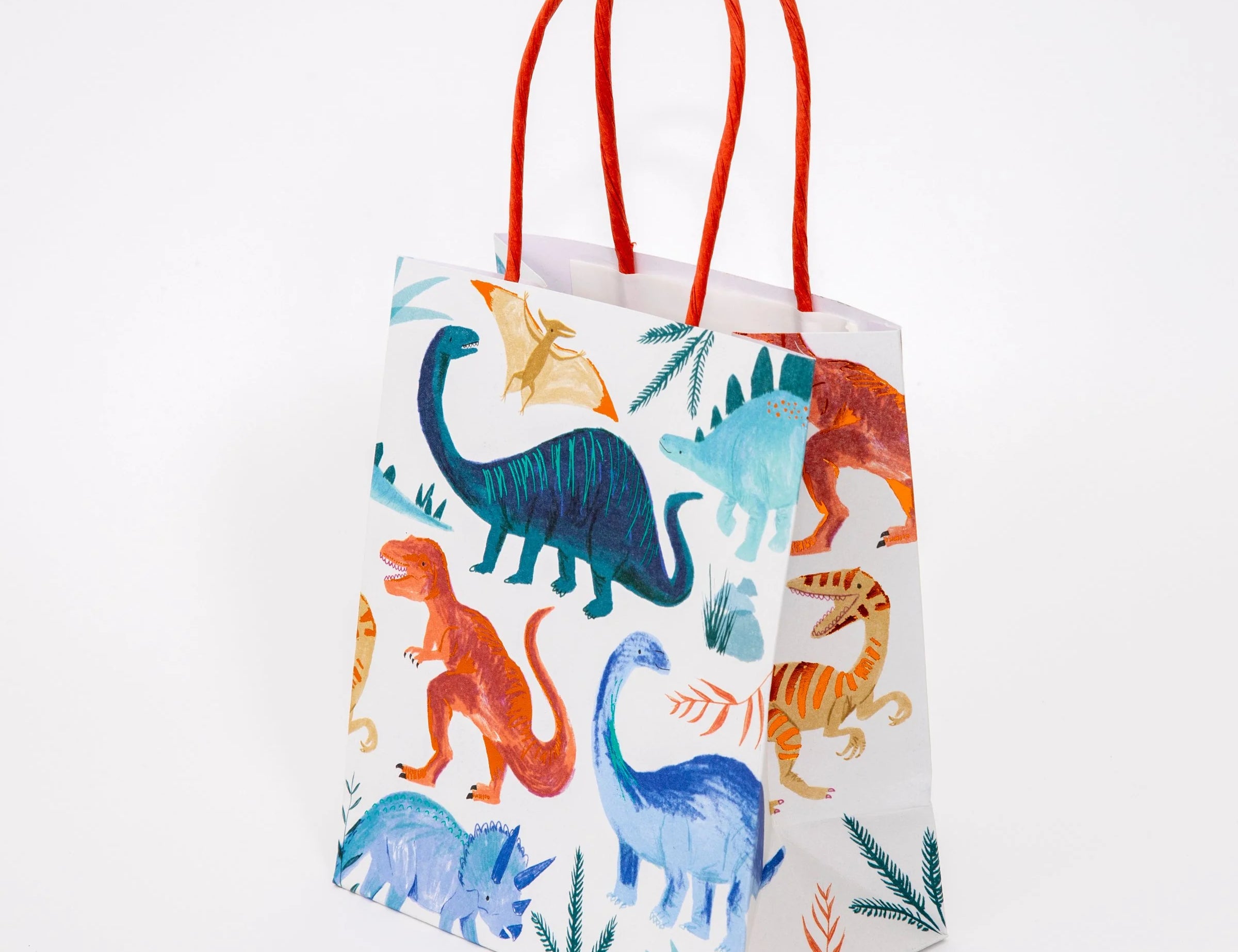 Meri Meri Dinosaur Kingdom Party Bag, a cream paper bag with colorful dinosaurs and red rope handles