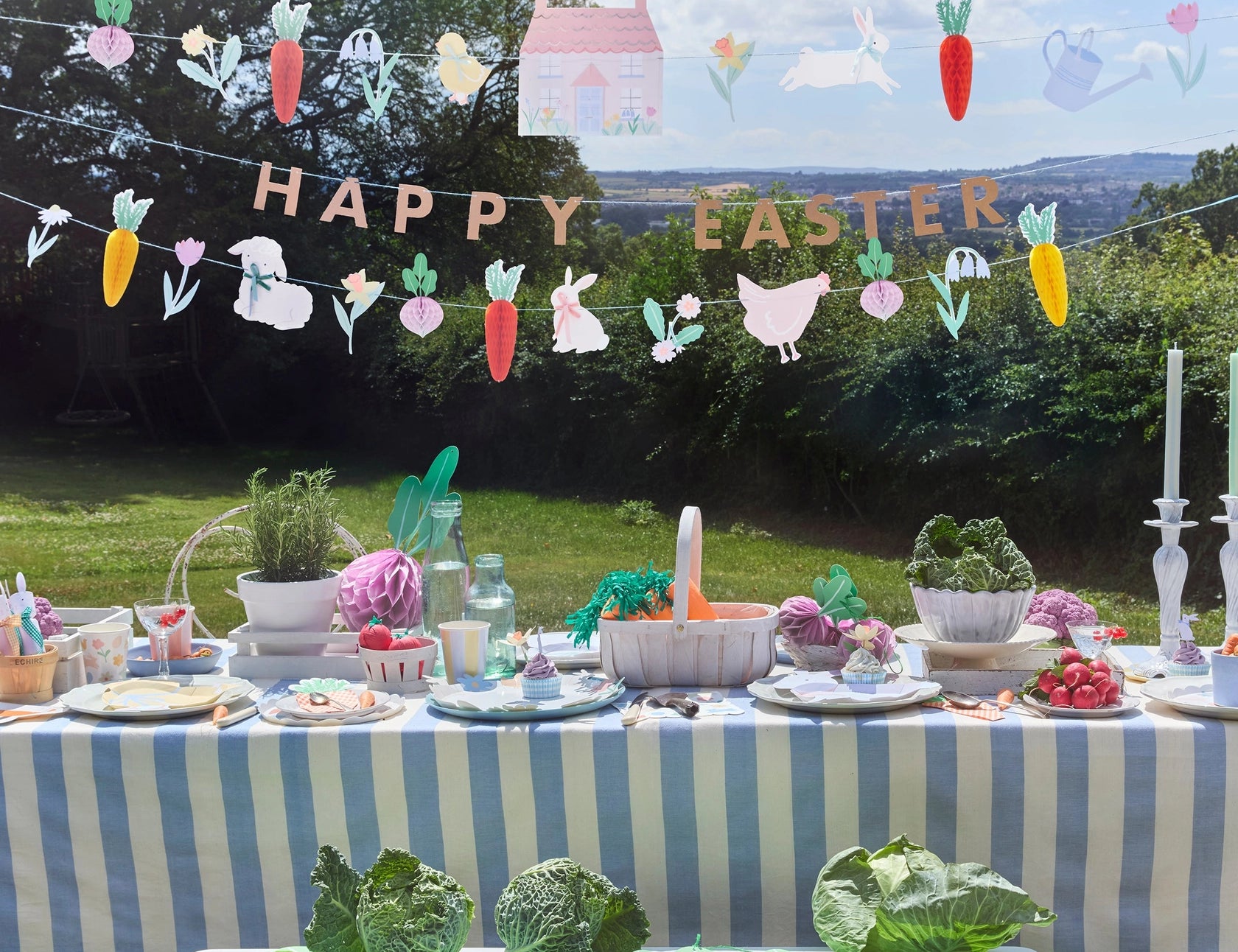 Meri Meri Easter Vegetable Garden Garland Set hung over an outdoor Easter table with cabbages and flowers