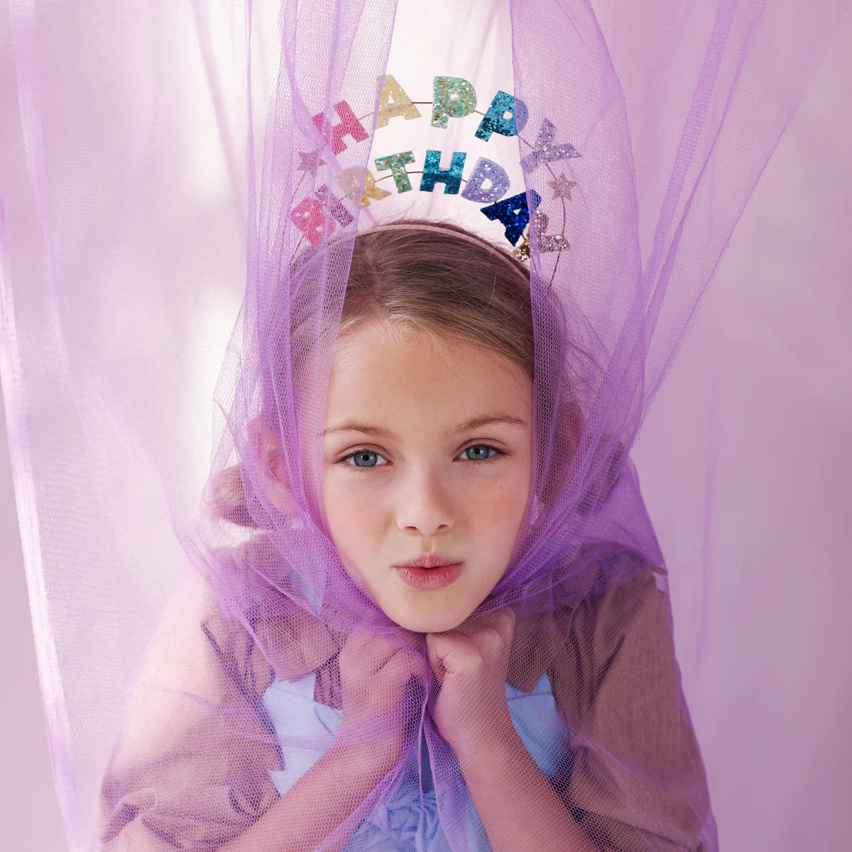 Girl under a purple tulle canopy wearing the Meri Meri Happy Birthday Glitter Headband