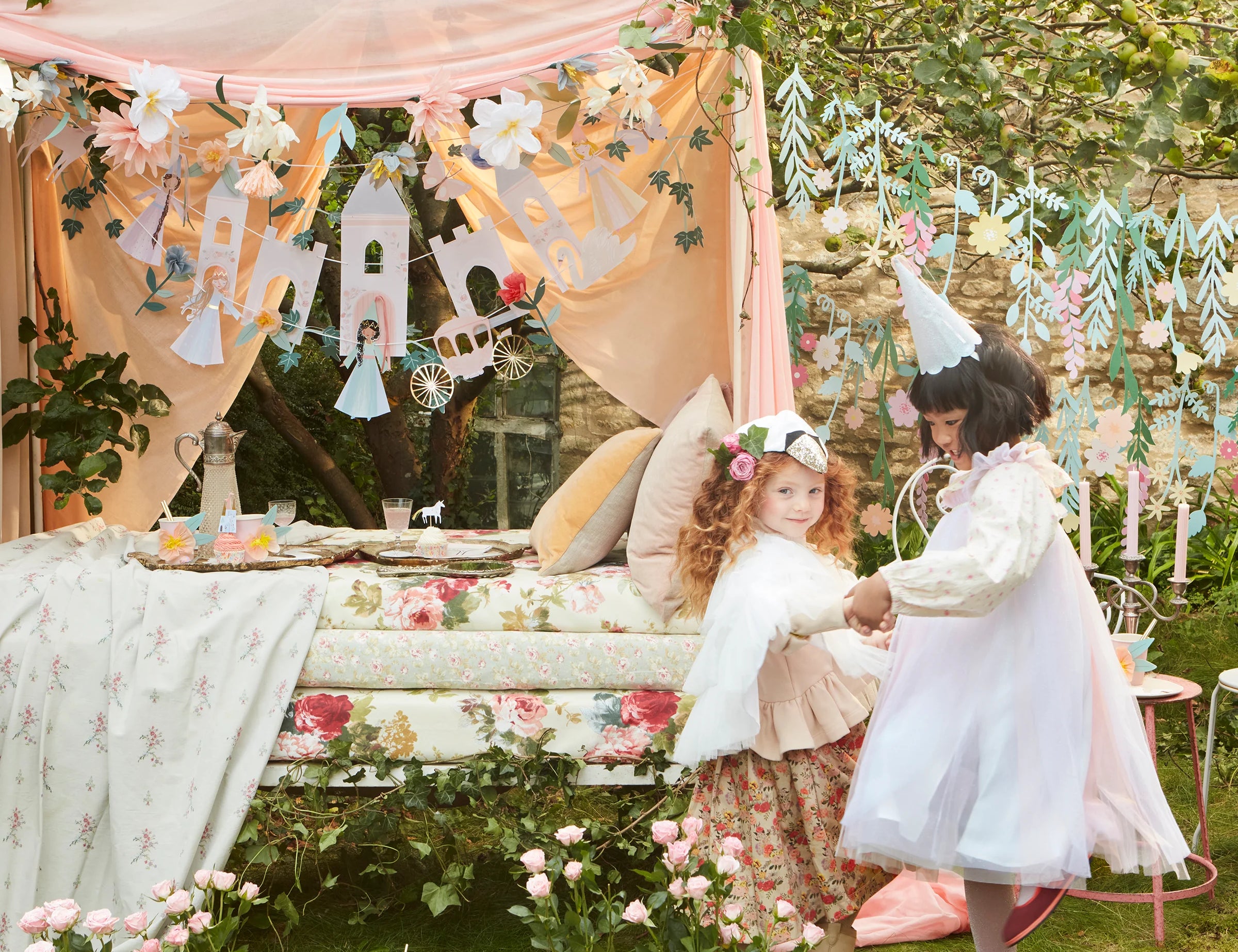 Two girls in princess dresses at a garden party decorated with the Meri Meri Princess Party Garland
