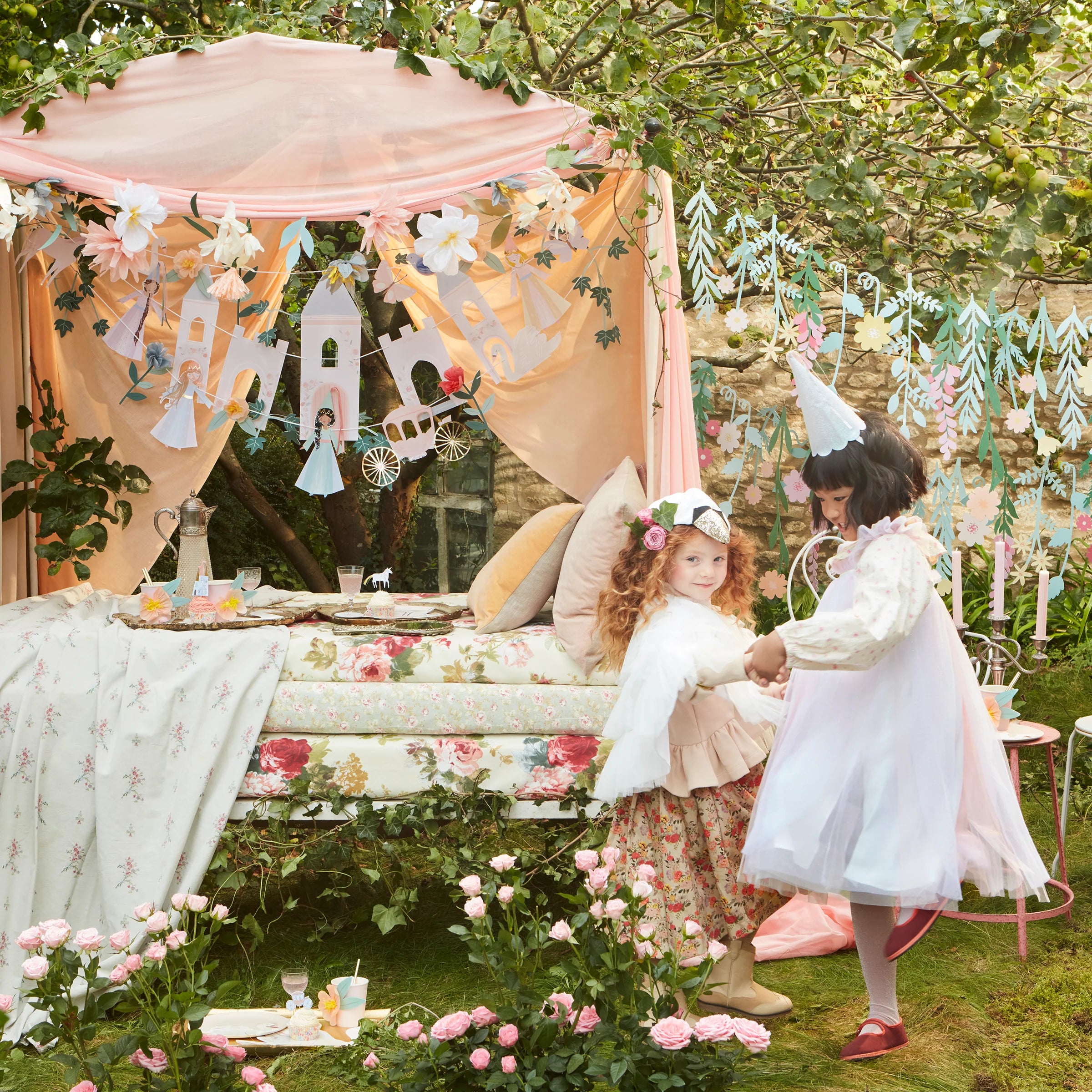 Two girls in princess dresses at a garden party decorated with the Meri Meri Princess Party Garland