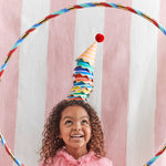 Smiling girl wearing a Meri Meri Stripe Party Hat under a rainbow hoop at a party