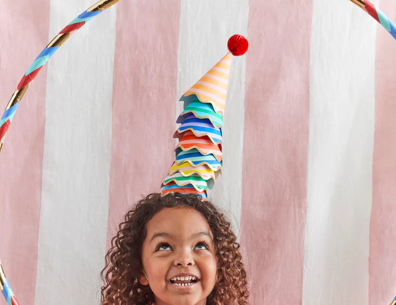 Smiling girl wearing a Meri Meri Stripe Party Hat under a rainbow hoop at a party